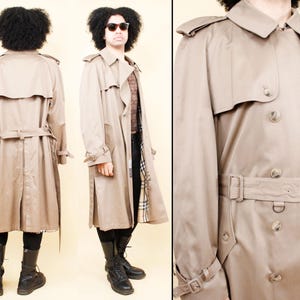 Puede incluir: Un abrigo tipo gabardina de color beige con diseño de doble botonadura, cinturón en la cintura y detalles de botones. Cuenta con charreteras y puños ajustables. El forro tiene un estampado de cuadros. Una prenda de abrigo clásica.