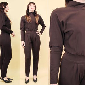 Op de afbeelding: Een bruine jumpsuit met een mock neck en lange mouwen. De jumpsuit heeft een aansluitend bovenlichaam en wijde broekspijpen.