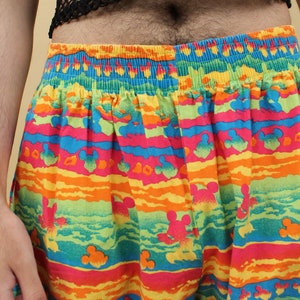May include: Colorful patterned shorts with a horizontal stripe design featuring Mickey Mouse silhouettes. The shorts have an elastic waistband.