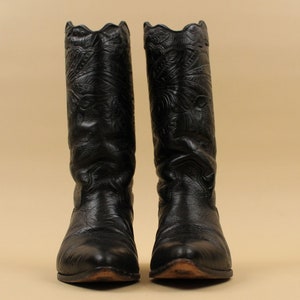 May include: A pair of black leather cowboy boots with intricate floral embroidery. The boots have a pointed toe and a tall shaft.