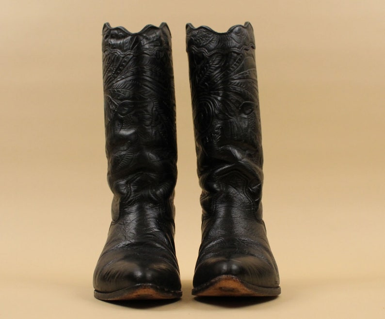 May include: A pair of black leather cowboy boots with intricate floral embroidery. The boots have a pointed toe and a tall shaft.