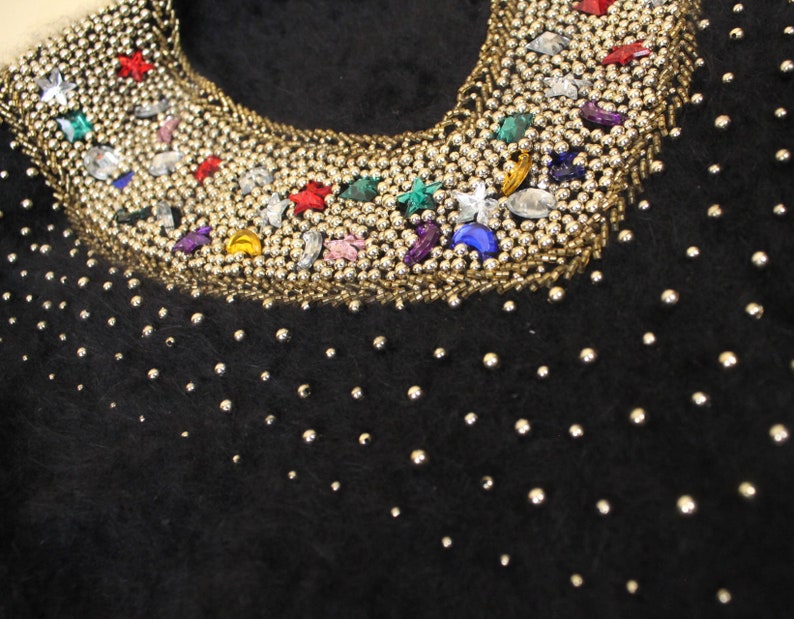 May include: Black fuzzy sweater with a silver beaded neckline decorated with colorful rhinestones and stars.