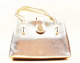 May include: A metallic gold handbag with a single strap and a decorative clasp. The bag has a smooth, shiny finish.