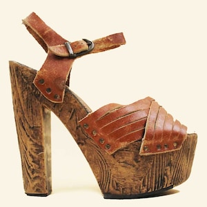May include: Brown leather platform sandals with a wooden heel and a buckle closure. The sandals have a woven leather strap across the toes.