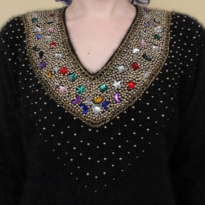 May include: A black fuzzy sweater with a V-neck and a beaded design. The beads are gold, silver, and multi-colored and form a pattern of stars, moons, and geometric shapes.