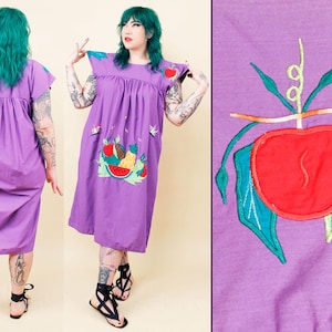 Może przedstawiać: Fioletowa bawełniana sukienka z haftowanymi wzorami owoców. Sukienka ma marszczony gorset i luźną, falującą spódnicę. Hafty przedstawiają arbuza, ananasa i inne owoce.