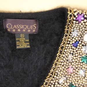 May include: Black angora rabbit hair and nylon blend cardigan with a beaded neckline featuring gold beads, rhinestones, and colorful stars. The label reads "CLASSIQUES" and "80% Angora Rabbit's Hair 20% Nylon Made in Hong Kong RN 58665 See Reverse for Care".