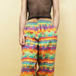 May include: A person wearing a black mesh tank top, colorful patterned pants, and black boots. The pants have a bright, multi-colored pattern with a geometric design.