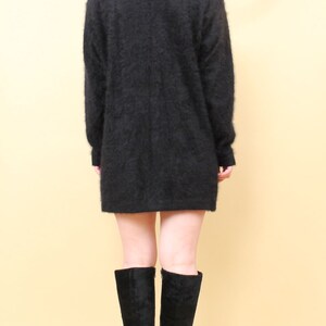 May include: A black fuzzy sweater with long sleeves and a loose fit. The sweater is worn over a pair of black knee-high boots with a platform heel.