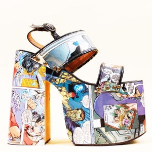 May include: Platform sandals with a comic book print. The open-toe shoes have a thick platform sole, a strap across the toes, and an ankle strap. The uppers are covered in colorful comic book panels with black accents and a buckle closure.