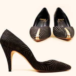 May include: Black high-heeled pumps with a unique wavy pattern and gold accents. The shoes have pointed toes and slender heels. The brand name "MILA" is visible inside the shoes.