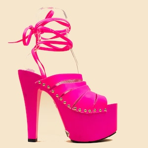 May include: A bright pink platform sandal with a high heel and a lace-up ankle strap. The sandal has a platform sole and a pointed toe.