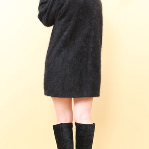 May include: A woman with blue hair is wearing a black fuzzy sweater and black knee-high boots with high heels.
