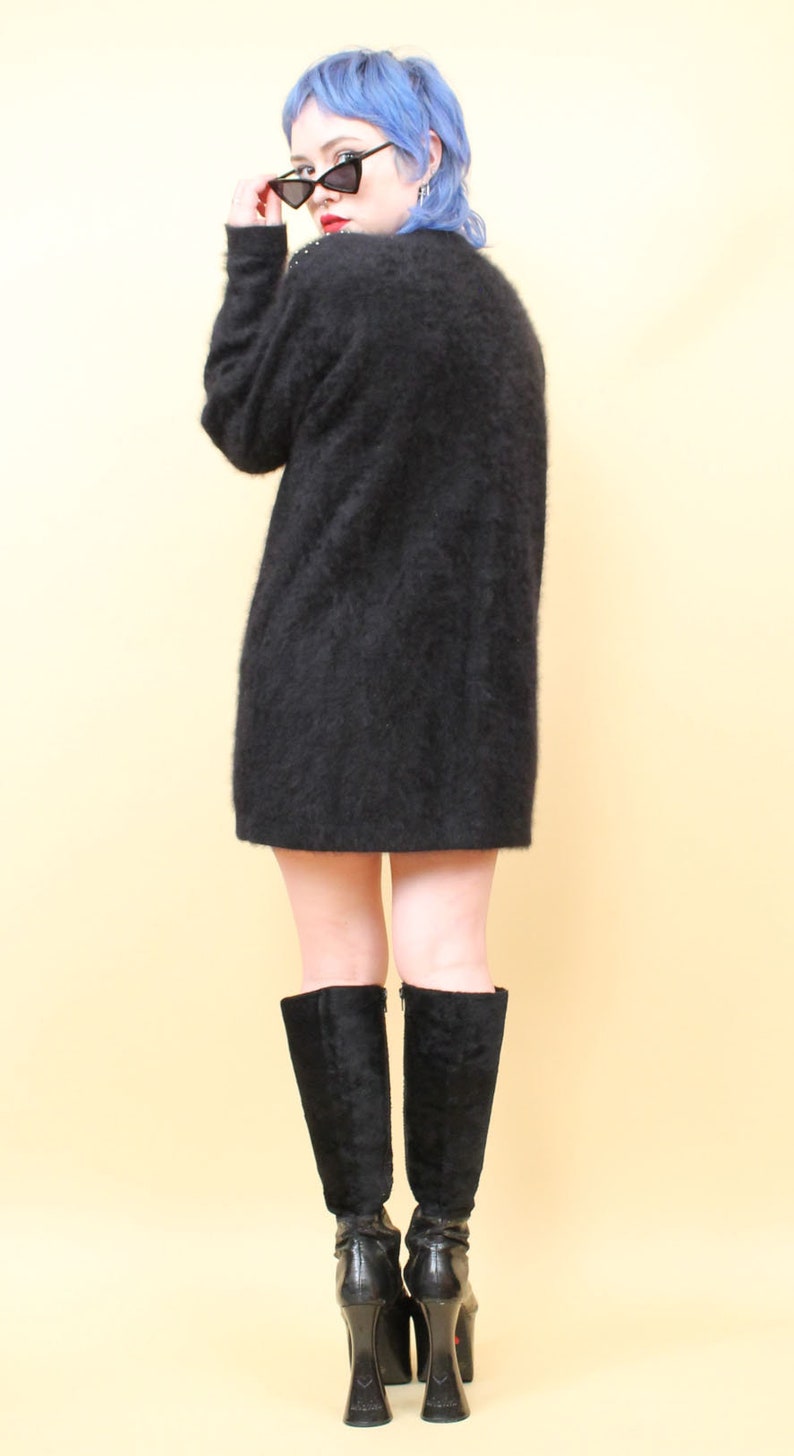 May include: A woman with blue hair is wearing a black fuzzy sweater and black knee-high boots with high heels.