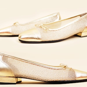 May include: Gold-colored mesh flats with a pointed toe and small bow detail. The toe and heel are solid gold. The shoes have a low heel and a black sole. The shoes are displayed on a light beige background.