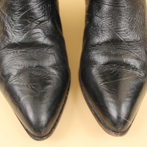 May include: A pair of black leather cowboy boots with pointed toes. The boots are made of a smooth, textured leather.