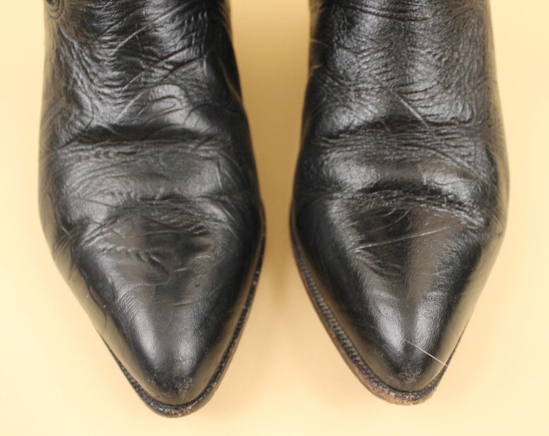 May include: A pair of black leather cowboy boots with pointed toes. The boots are made of a smooth, textured leather.