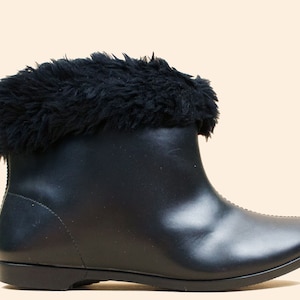 May include: Black ankle boot with a faux fur trim. The boot features a smooth, matte finish and a low heel. The fur trim adds a touch of luxury to this stylish footwear. A versatile boot for various occasions.