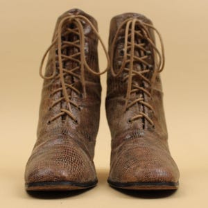 May include: A pair of brown leather lace-up boots with a textured finish. The boots have a pointed toe and a low heel.