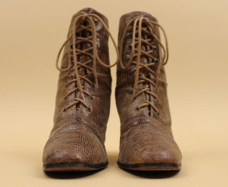 May include: A pair of brown leather lace-up boots with a textured finish. The boots have a pointed toe and a low heel.