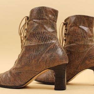 May include: A pair of brown leather ankle boots with lace-up fronts and block heels. The boots have a textured, snakeskin-like pattern.