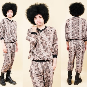 Puede incluir: Conjunto vintage de dos piezas con un diseño estampado en tonos marrones y beige. La parte superior tiene cuello en V y ribete negro, combinado con pantalones a juego. El conjunto se completa con botas negras. El atuendo se muestra desde múltiples ángulos.