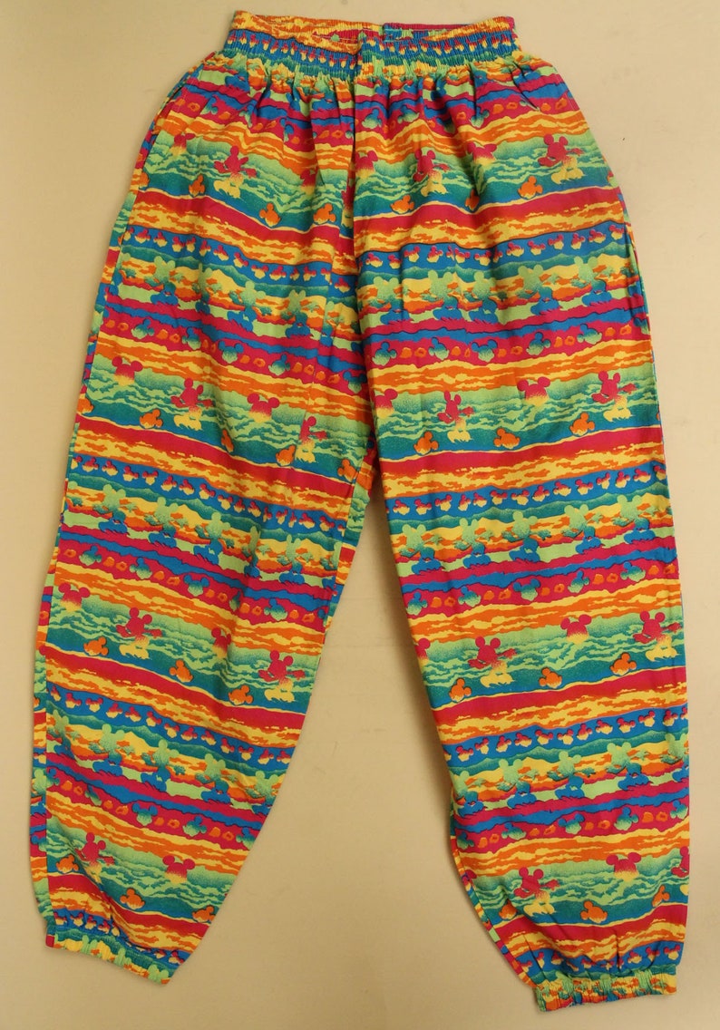 May include: Multicolored pants with a striped pattern featuring a repeated design of Mickey Mouse heads. The pants have an elastic waistband and a relaxed fit.