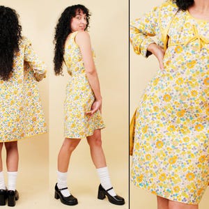 May include: A vintage-style outfit featuring a floral print dress and matching coat. The dress is sleeveless with a scoop neckline, and the coat is long-sleeved. Both garments have a yellow, white, and blue floral pattern. The outfit is paired with black shoes.