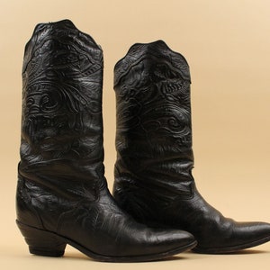 May include: A pair of black leather cowboy boots with intricate floral embroidery. The boots have a pointed toe and a low heel.