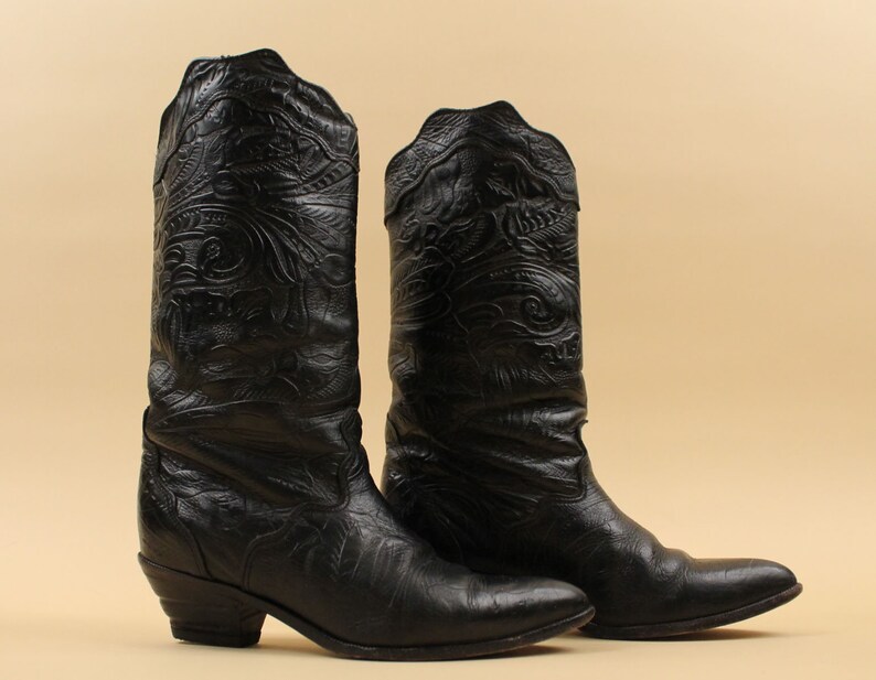 May include: A pair of black leather cowboy boots with intricate floral embroidery. The boots have a pointed toe and a low heel.