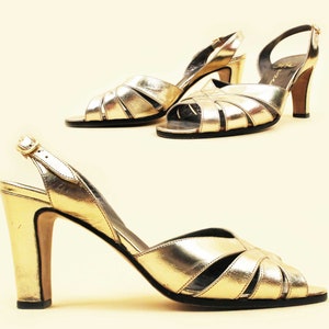 May include: A pair of gold heeled sandals with a slingback strap and open toe design. The sandals have a criss-cross pattern on the front and a block heel.