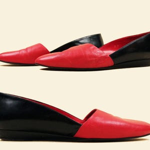 May include: A pair of black and red leather heeled flats. The shoes have a pointed toe and a low heel. The shoes are made of a smooth leather and have a contrasting color design.