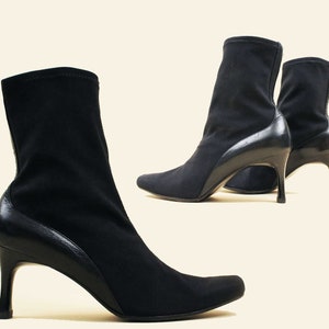 May include: A pair of black heeled ankle boots with a stretchy fabric upper and a leather heel counter. The boots have a pointed toe and a stiletto heel.
