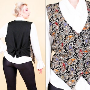 May include: A black waistcoat featuring a colourful paisley design in red, orange, blue, and gold. The waistcoat has a V-neck and button closure. The back is plain black with a tie. It is worn over a white long-sleeved shirt.