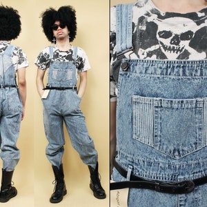 May include: A light blue denim overall with a black belt and a skull graphic on the front. The overall has a large pocket on the front and a smaller pocket on the right side.