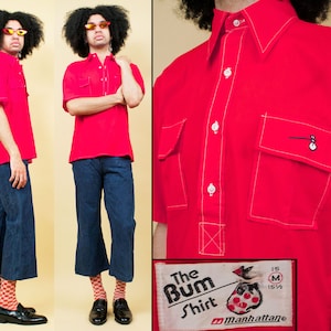 May include: A red short-sleeved shirt with two large pockets and white stitching. The shirt has a button-up front and a collar. The text "The Bum Shirt" and "Manhattan" is printed on the bottom of the shirt.