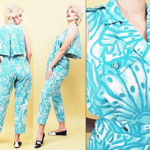 Op de afbeelding: Een turquoise en wit gepatroneerde jumpsuit met een gekraagde top en een mouwloos ontwerp. De jumpsuit heeft een wijde pijp en een cropped top.
