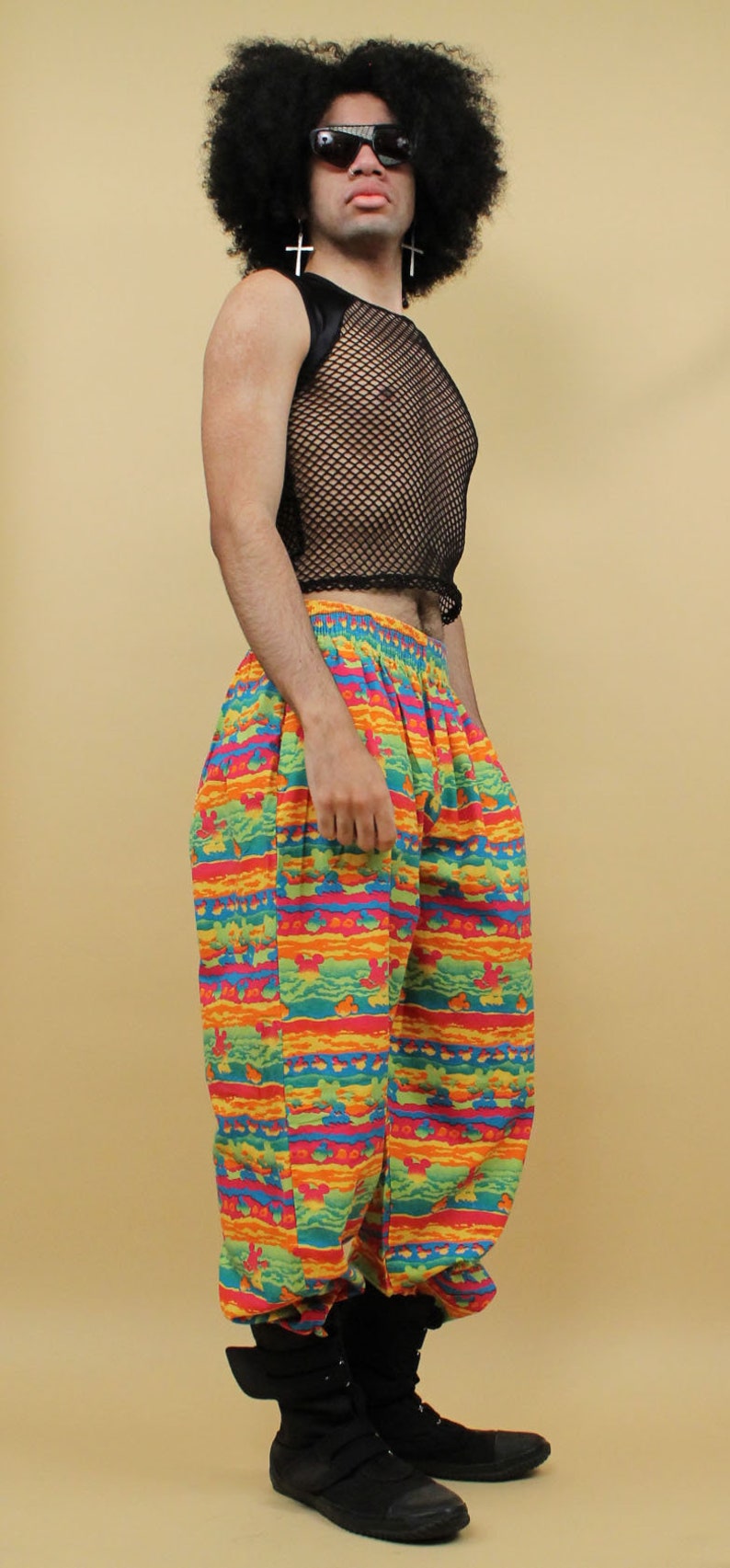 May include: A person wearing a black mesh tank top, colorful patterned pants, and black boots. The person is wearing sunglasses and has an afro.