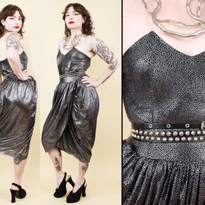 May include: A strapless metallic silver and black speckled midi dress featuring a sweetheart neckline and a draped skirt. The dress is cinched at the waist with a thin black leather belt and a wider black leather belt adorned with silver metal studs.