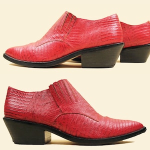 May include: A pair of red leather ankle boots with a pointed toe and a low heel. The boots have a textured, snakeskin-like pattern.