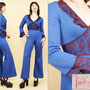 Op de afbeelding: Een blauwe jumpsuit met lange mouwen en wijde pijpen. De jumpsuit heeft bruine kantversiering rond de halslijn, manchetten en taille. Het model draagt de jumpsuit met zwarte plateauhakken. De afbeelding bevat de tekst "fredericks' of hollywood".