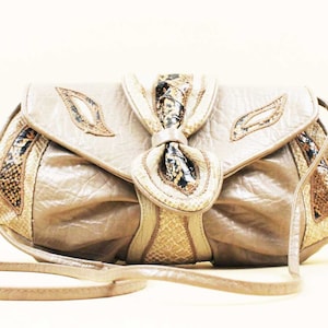 May include: A beige leather clutch bag with a snakeskin pattern and a bow detail. The bag has a long strap.