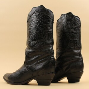 May include: A pair of black leather cowboy boots with intricate embossed designs. The boots have a pointed toe and a low heel.