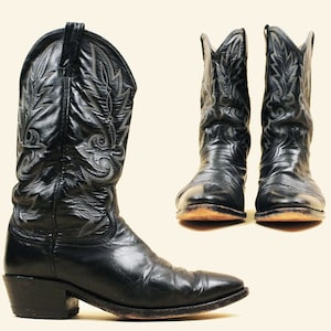 Op de afbeelding: Een paar zwarte leren cowboylaarzen met ingewikkelde borduursels. De laarzen hebben een spitse neus en een hoge hak.