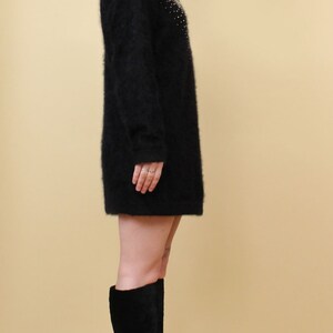 May include: A black fuzzy sweater with a gold embellishment and a woman wearing black platform boots.