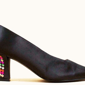 May include: Black satin pumps with a low block heel. The heel is covered in colorful rhinestones.