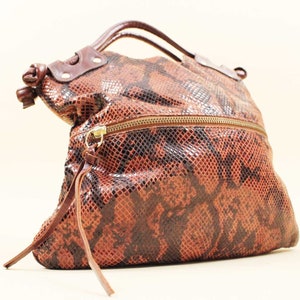 Puede incluir: Un bolso de mano de cuero marrón con estampado de piel de serpiente. El bolso tiene una cremallera y un asa superior.