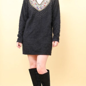 May include: A black fuzzy sweater with a jeweled neckline. The sweater has a v-neck and is worn with black knee-high boots.