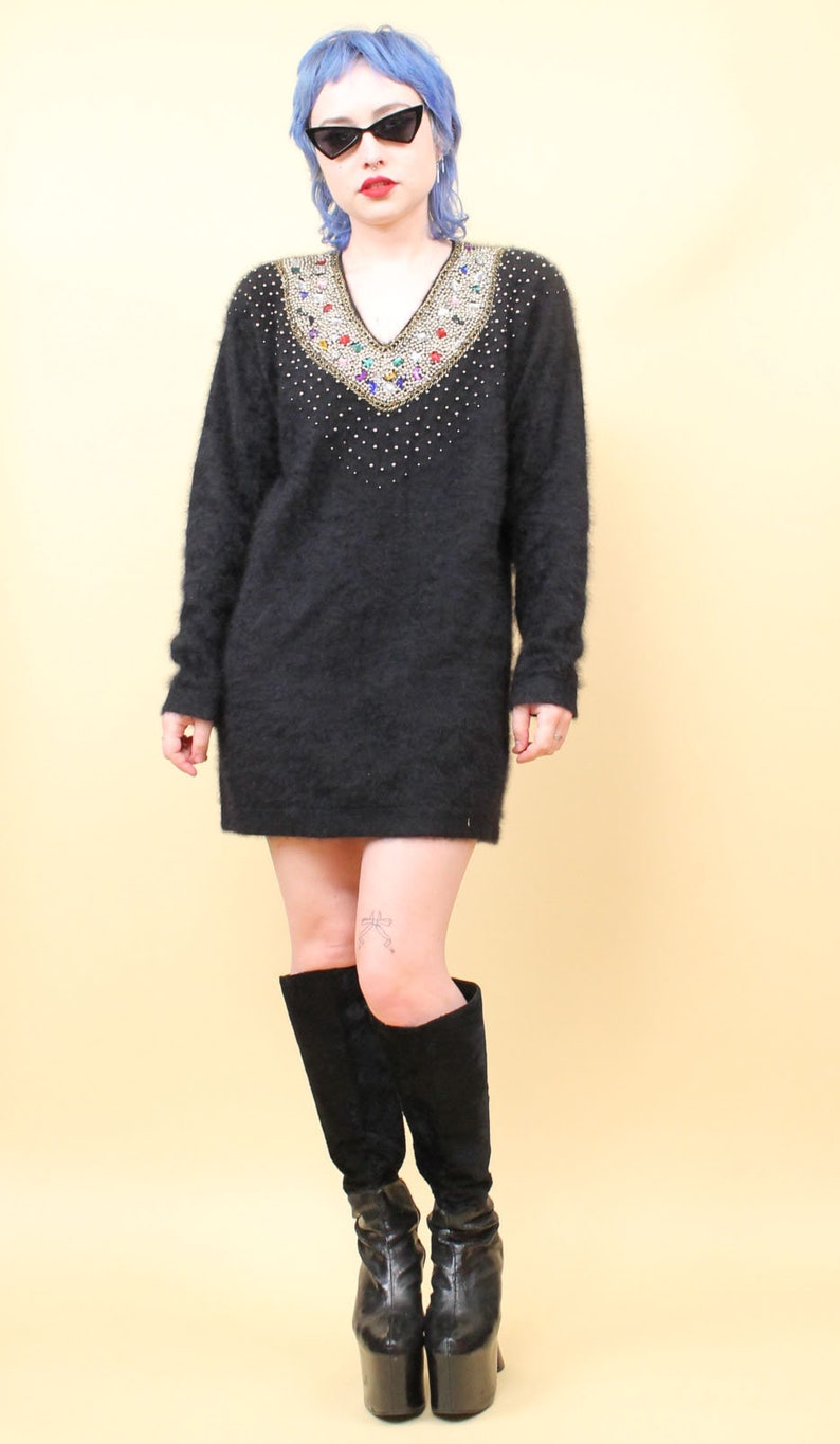 May include: A black fuzzy sweater with a jeweled neckline. The sweater has a v-neck and is worn with black knee-high boots.