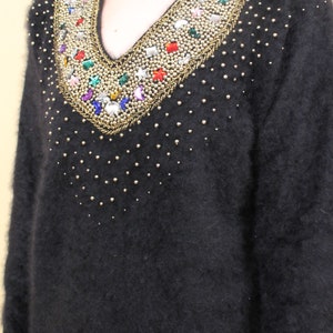 May include: A black fuzzy sweater with a v-neck and a decorative beaded neckline featuring colorful rhinestones and gold accents.